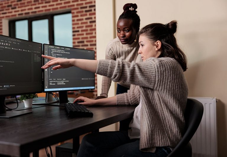 Dos personas trabajando en un ordenador de sobremesa con dos monitores